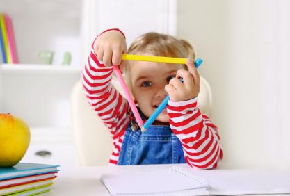 Un enfant forme un triangle avec trois gros crayons de couleur