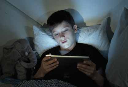 Un jeune garçon regarde sa tablette dans son lit