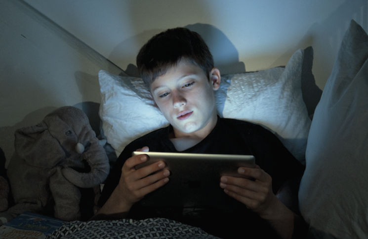 Un jeune garçon regarde sa tablette dans son lit
