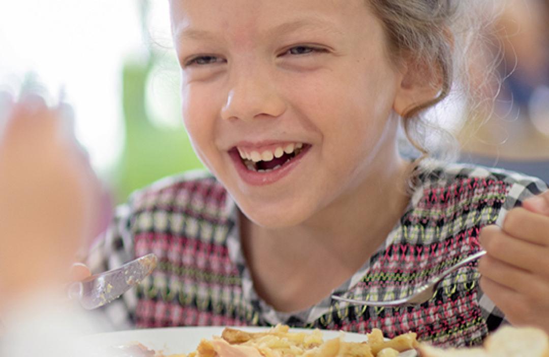 Fille souriant devant une assiette à la cantine